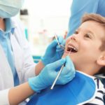 Leczenie mleczaków - dentysta badający zęby u leżącego na fotelu stomatologicznym chłopca
