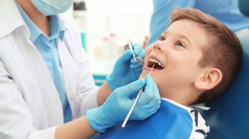 Leczenie mleczaków - dentysta badający zęby u leżącego na fotelu stomatologicznym chłopca