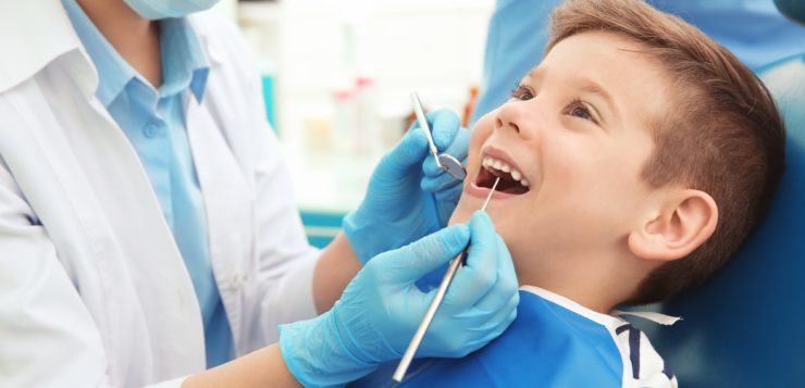 Leczenie mleczaków - dentysta badający zęby u leżącego na fotelu stomatologicznym chłopca